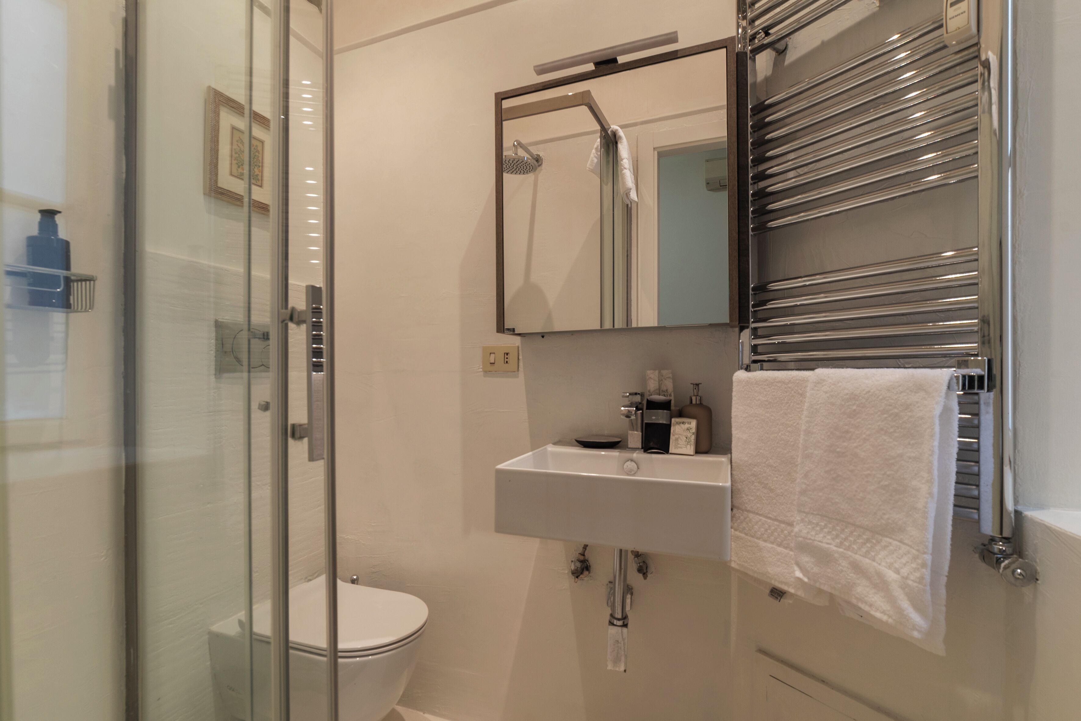 A modern bathroom with a glass shower enclosure, a white toilet, a sink with a mirror above it, and a towel rack.