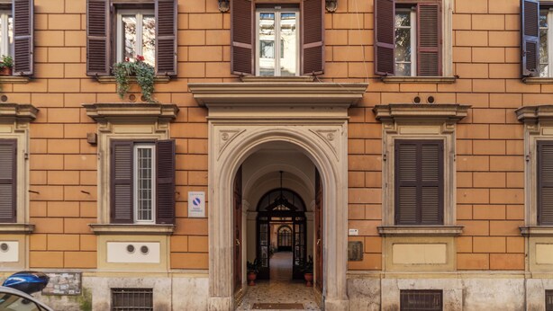 Eine Gebäudefassade mit zahlreichen Fenstern, davon einige mit Fensterläden, und einem zentralen Eingang mit Bogen.