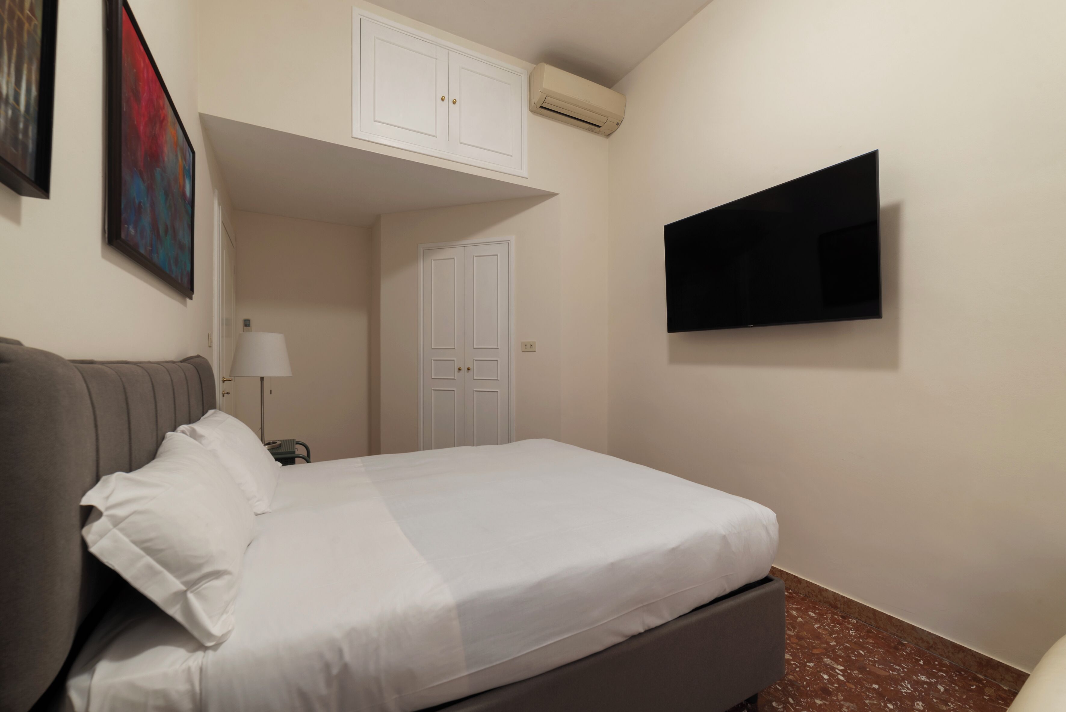 A hotel room with a bed, a TV mounted on the wall, a wardrobe, and a door.