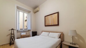 Ein Hotelzimmer mit Bett, Nachttisch mit Lampe, Fenster mit Blick und Wandbild.