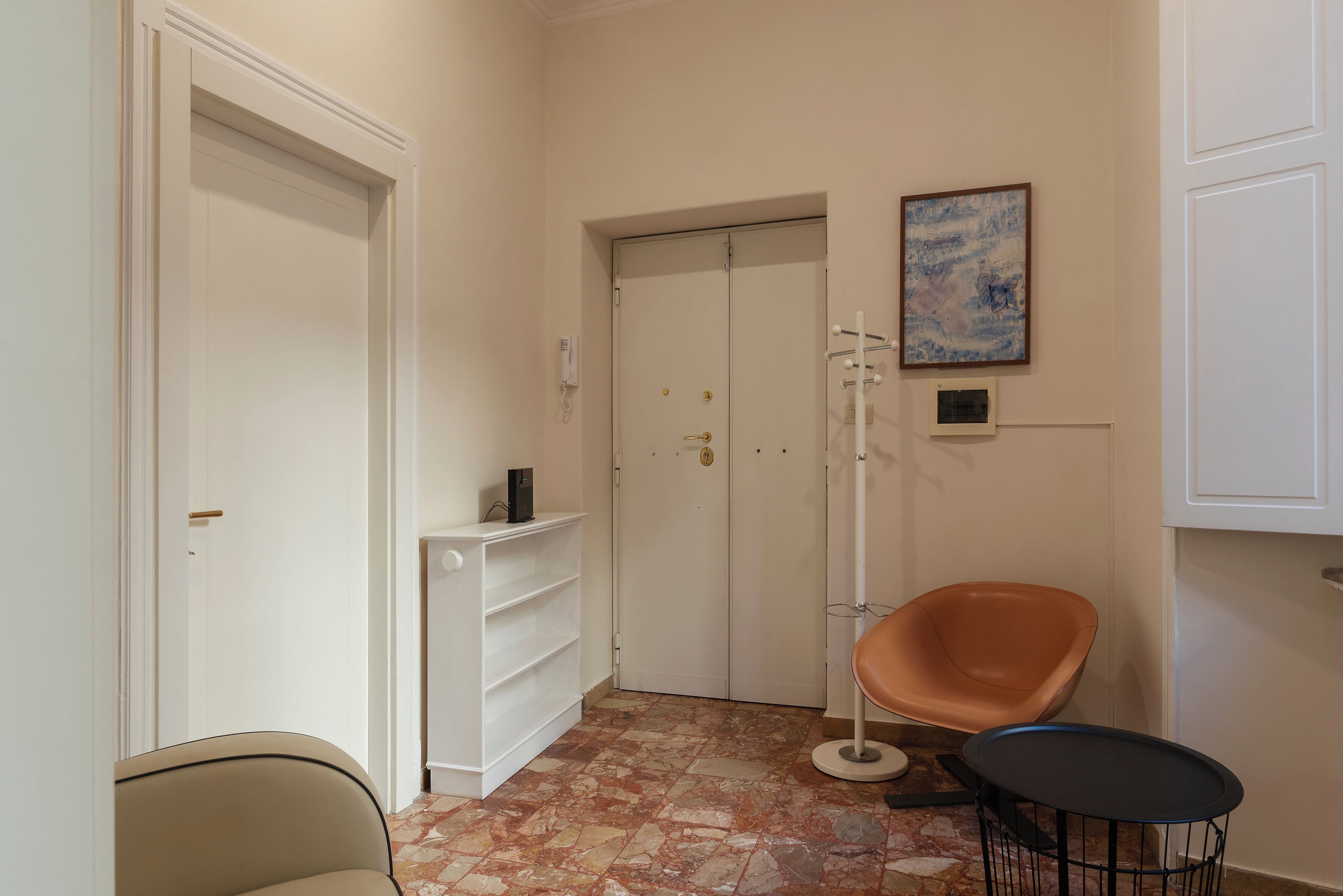 A hallway with a white door, a white shelving unit, a tall floor lamp, and a single orange chair.
