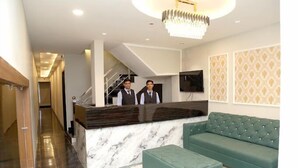 A hotel reception area with a marble counter, a green sofa, and a staircase in the background. - JMC HOTEL STAR INN (Indore)