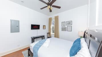 A hotel room with a bed, a ceiling fan, a TV, a desk, and a window with curtains.