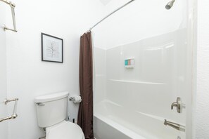Een badkamer met een toilet, een ingelijst foto aan de muur, een douchegordijn en een bad.
