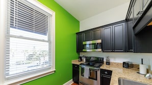 A kitchen with a green wall, stainless steel appliances, and black cabinets.