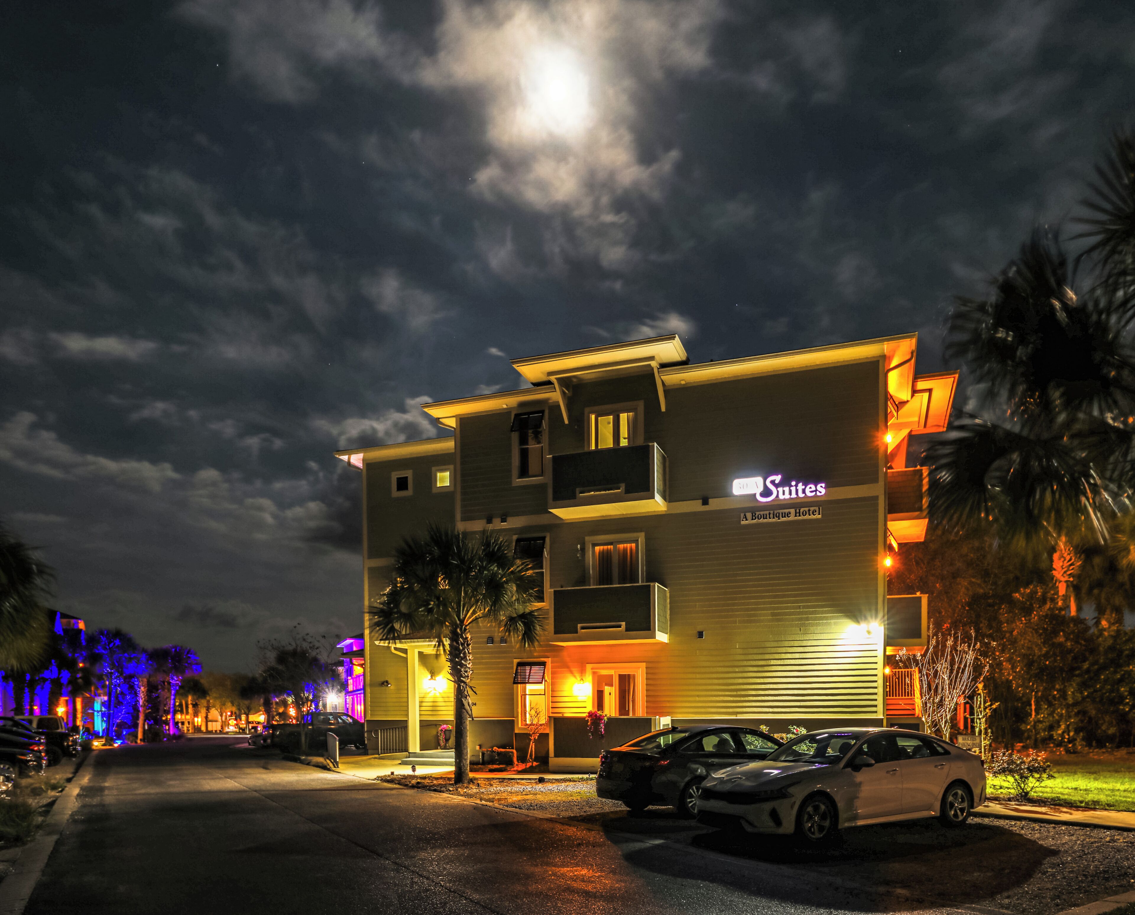 A hotel with a sign reading "Suites Boutique Hotel" and two cars parked in front.