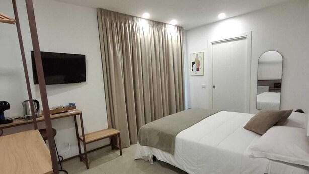 Ein Hotelzimmer mit Bett, Schreibtisch mit Stuhl, Wandfernseher, Spiegel und einem Vorhangfenster.