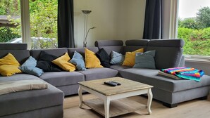 A modern living room with a grey sectional sofa, a small wooden coffee table, and a colorful blanket on the right armrest. - Lovely family home in Laren (Laren)