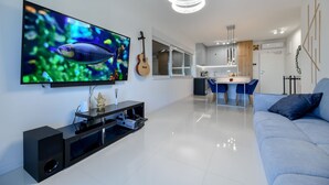 A modern living room with a flat-screen TV, a guitar, a dining area, and a blue sofa.