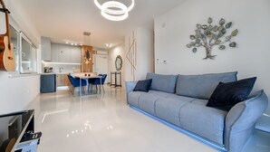 A modern living room with a grey sofa, a dining area with a table and chairs, and a kitchen in the background.