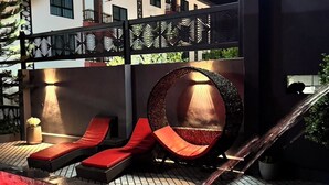 A modern outdoor pool area with red loungers, a circular seating area, and a staircase leading to an upper level. - Grand Pruksasiri Hotel Chaiyaphum (Chaiyaphum)