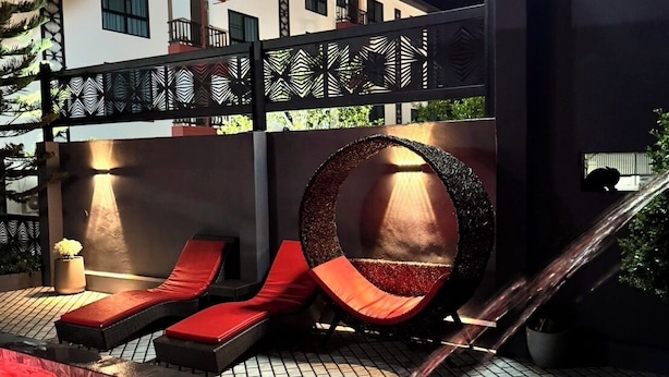A modern outdoor pool area with red loungers, a circular seating area, and a staircase leading to an upper level.