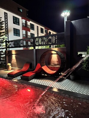 A modern outdoor pool area with red loungers, a circular seating area, and a staircase leading to an upper level. - Grand Pruksasiri Hotel Chaiyaphum (Chaiyaphum)