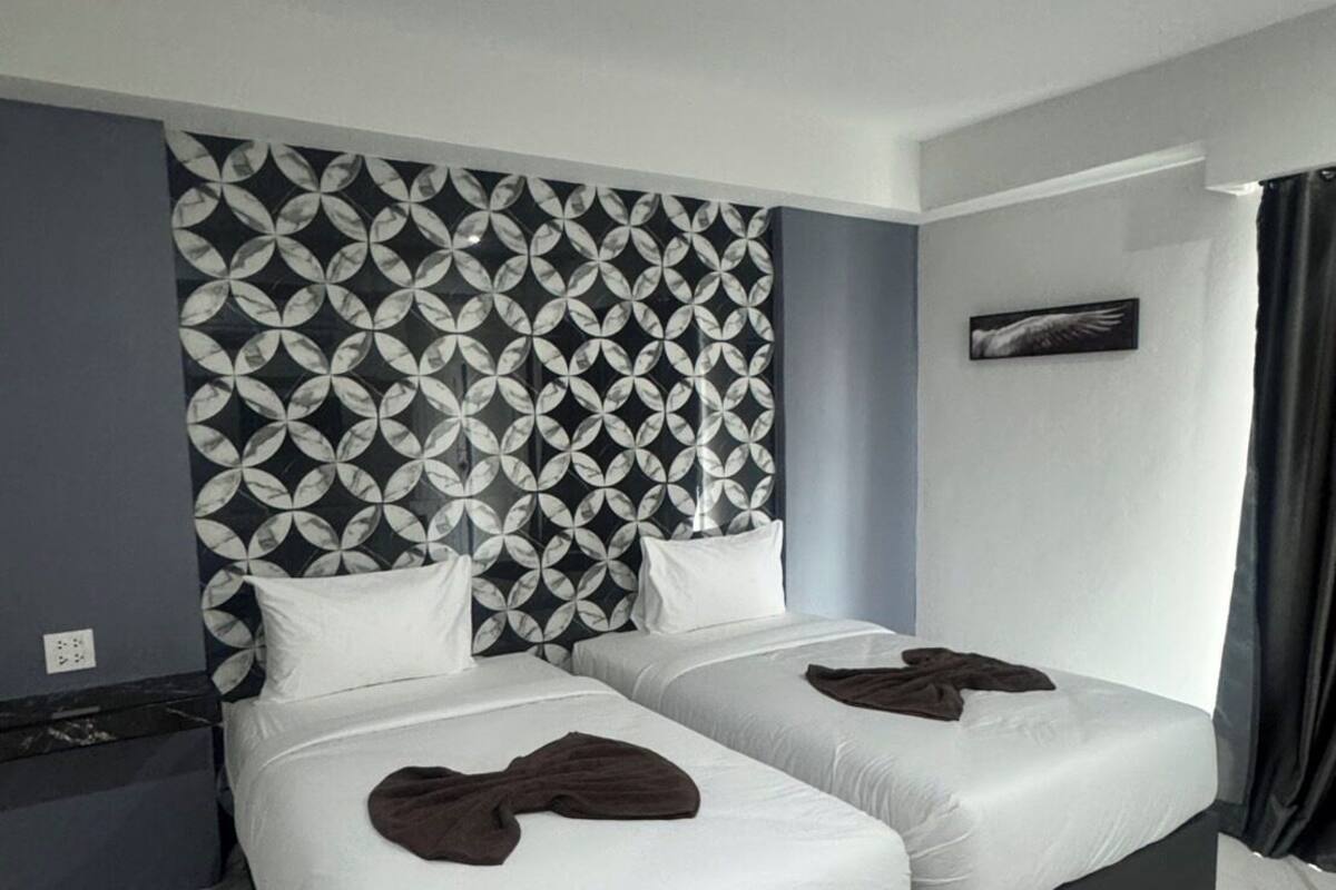 A hotel room with two beds, a patterned headboard, a nightstand, and a wall-mounted artwork.