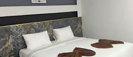 Une chambre d’hôtel moderne avec un grand lit, une tête de lit au motif de marbre, une table de chevet et un tableau encadré au mur.
