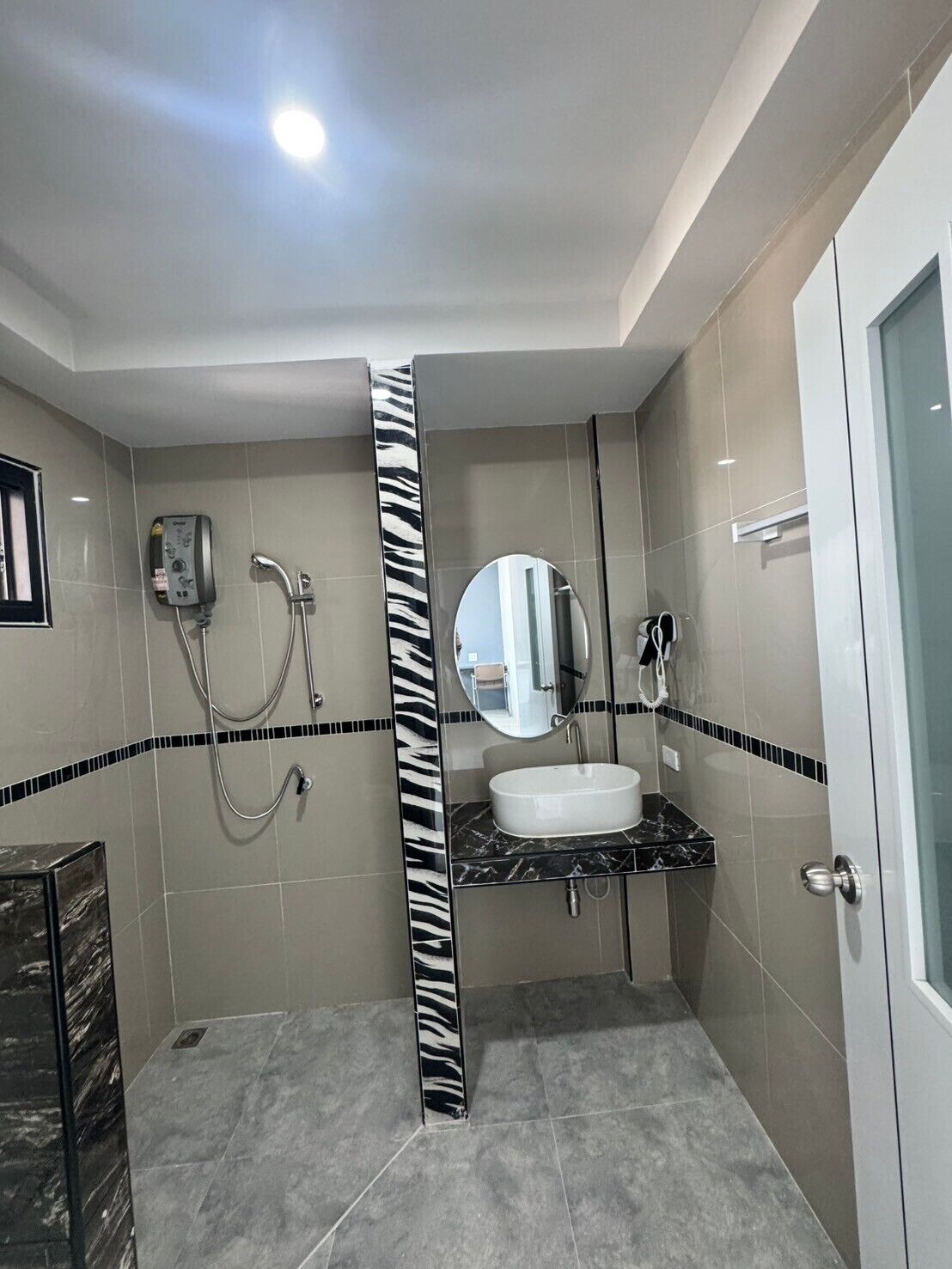 Une salle de bain moderne avec une colonne à rayures zébrées, un lavabo encastré et une douchette à main.