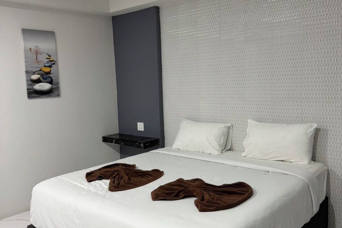 A modern hotel room with a large bed, white bedding, and a grey headboard.