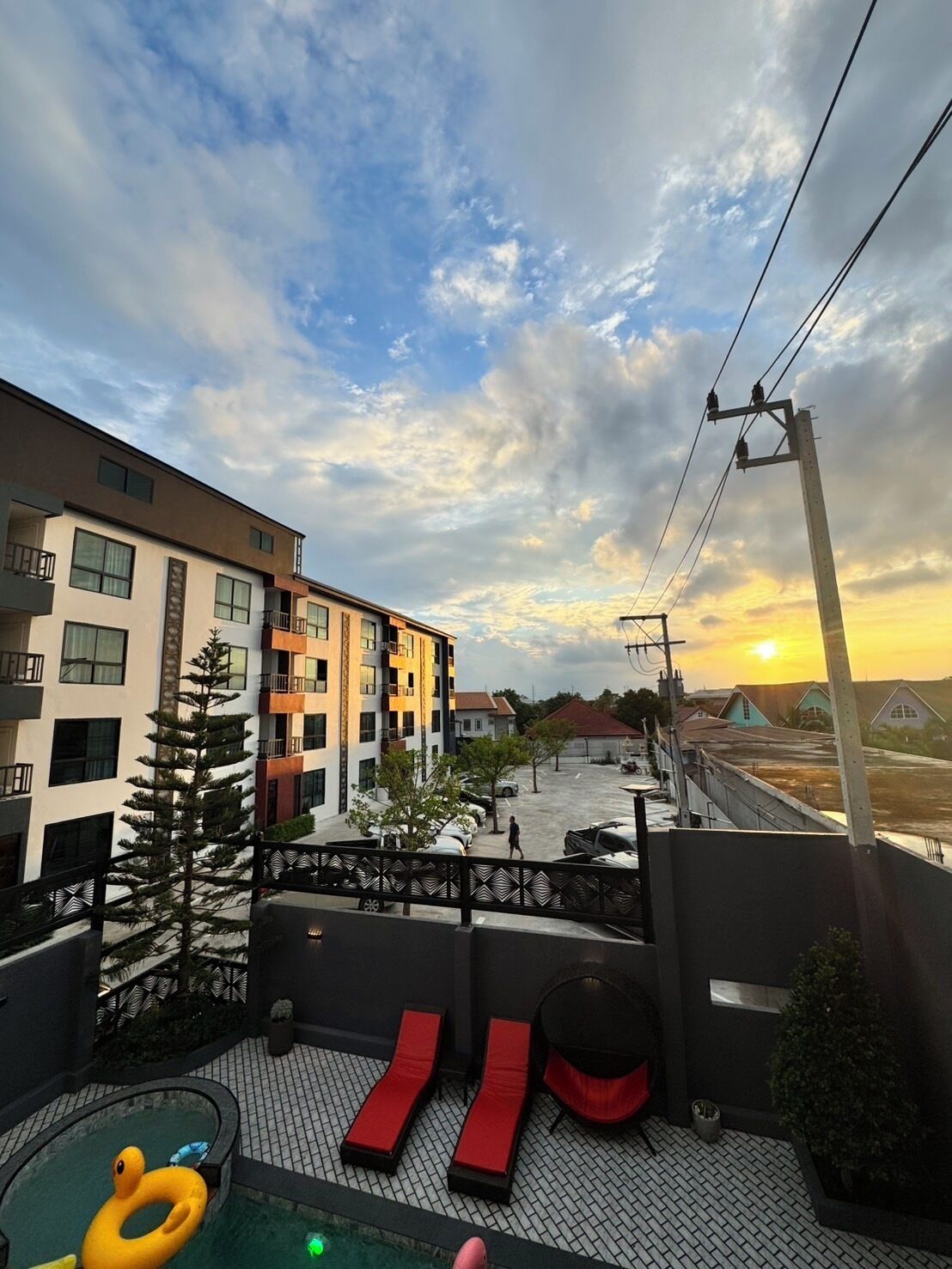 Zona de piscina en la azotea con sillas de descanso y una piscina inflable pequeña, con vista a un barrio residencial al atardecer.