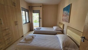 A bedroom with two beds, a wardrobe, a painting, and a window with curtains. - Albania Dream Holidays Apartment (Sarandë)