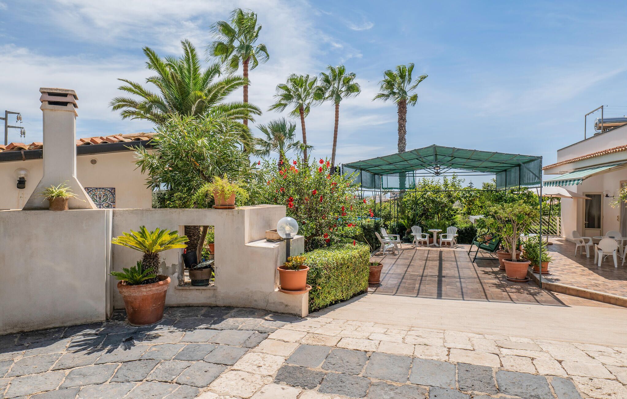 A courtyard with a covered seating area, potted plants, and palm trees.