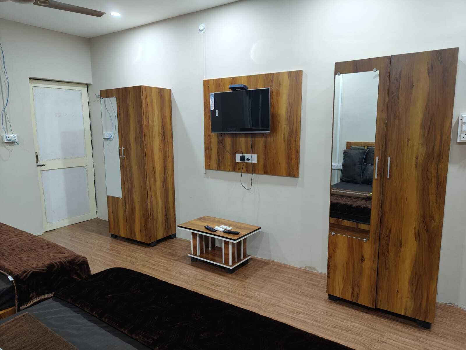 A room with a wooden wardrobe, a TV mounted on the wall, and a small table with a remote control.