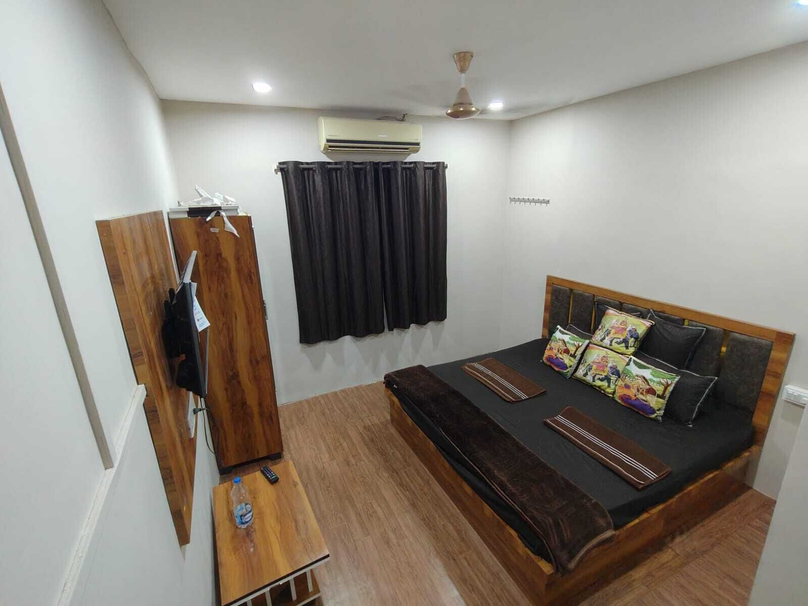 A bedroom with a bed, a wardrobe, a small table with a bottle, and an air conditioning unit.