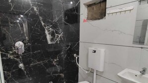 Een badkamer met een zwarte marmeren wand, een wit toilet, een wastafel en een roze emmer.