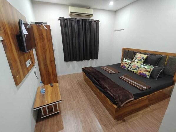 A bedroom with a wooden bed, a TV mounted on the wall, and a small wooden table with a remote control. - Shree Kedarnath Homestay in Ujjain (Ujjain)