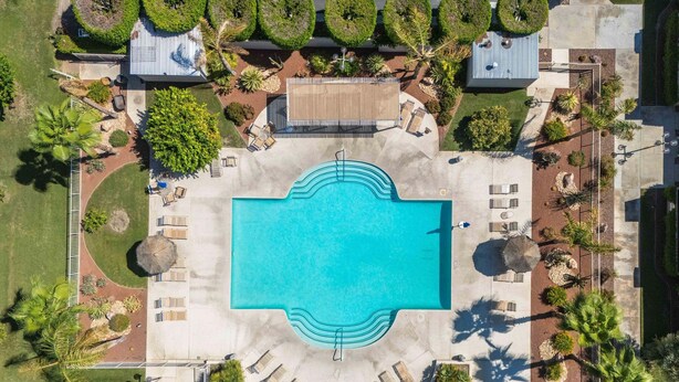Vista aérea de un resort con piscina central, áreas de descanso y jardines ajardinados.