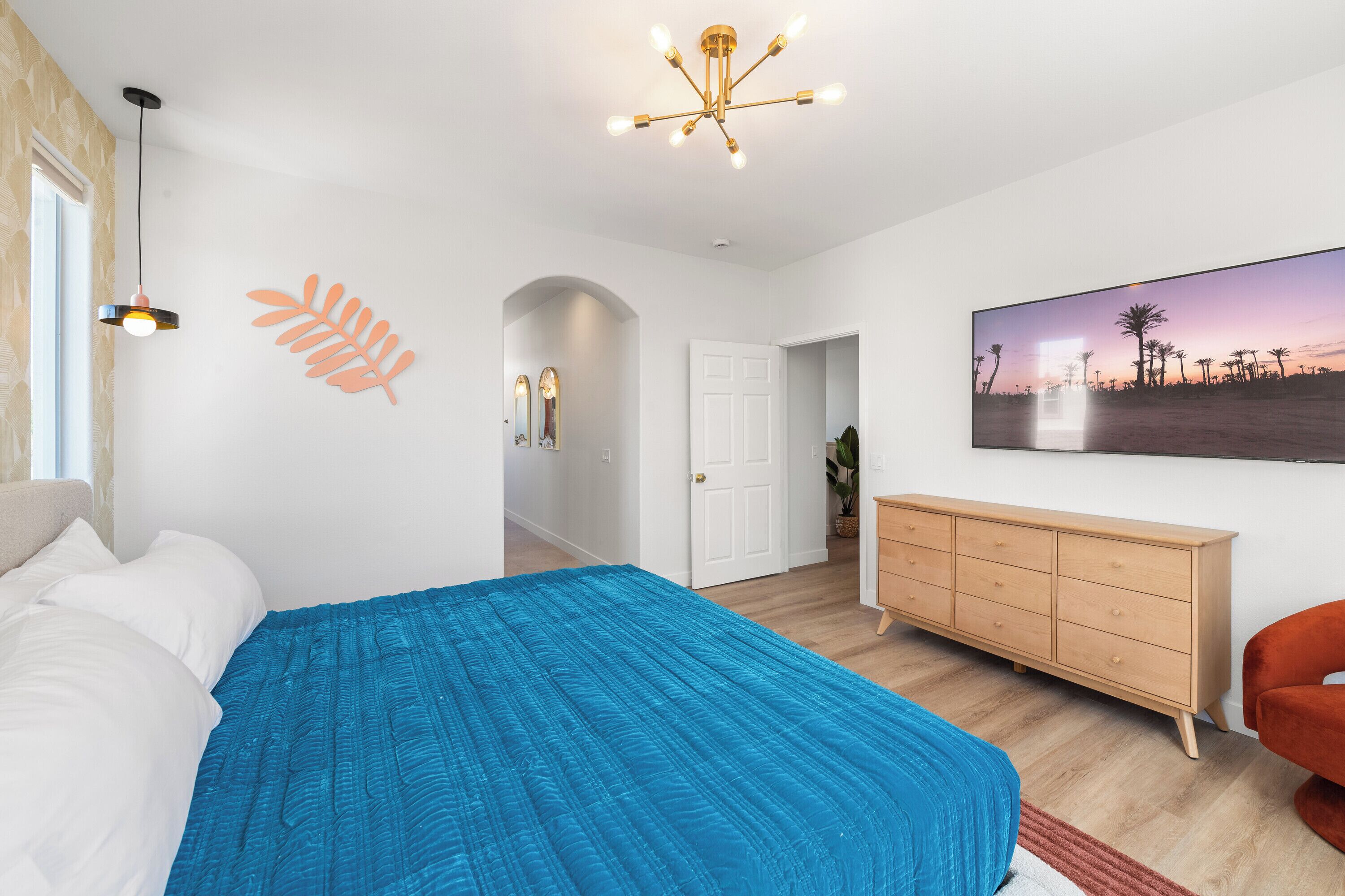 A bedroom with a large bed, a dresser, a painting, and a hallway leading to another room.