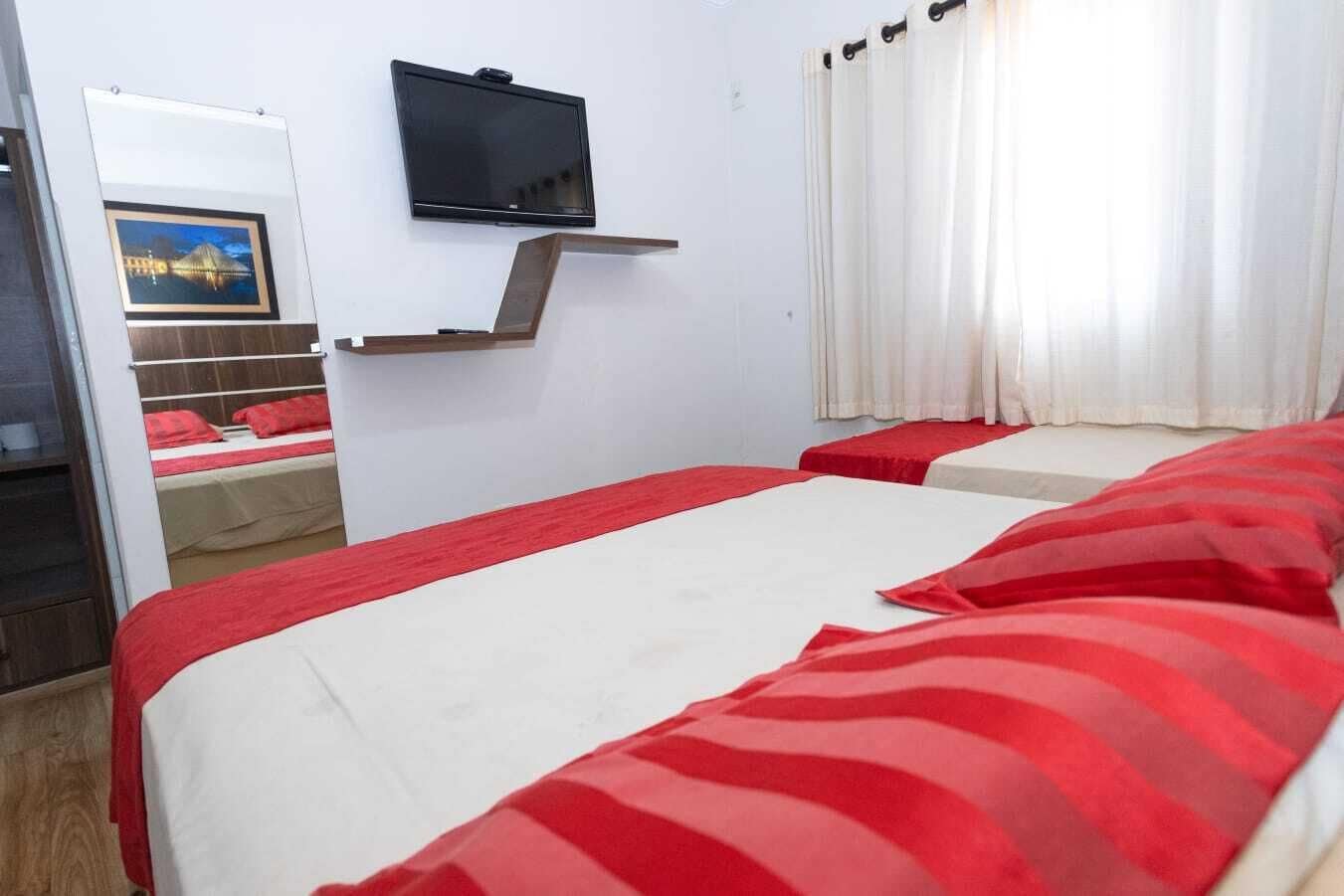 Ein Hotelzimmer mit zwei Betten, einem an der Wand montierten Fernseher und einem Fenster mit Vorhängen.