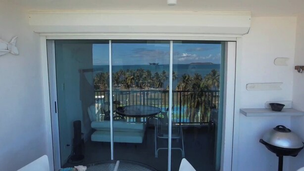 A balcony with a glass door, a small table, and a chair, overlooking a pool and palm trees. - Only by boat chic 2-bedroom apartment with AC, WiFi in private island in Fajardo (Fajardo)