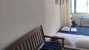 A room with a wooden bench, a bed with a blue mattress, a hanging plant, and a window with curtains. - Sea view on the beach avenue - Embaré - Santos (Embaré Santos)