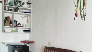 A compact living space with a wooden sofa, a small red stool, a black refrigerator, and a white tiled floor. - Sea view on the beach avenue - Embaré - Santos (Embaré Santos)