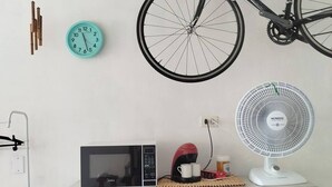 A room with a bicycle hanging on the wall, a clock, a microwave, and a fan on a shelf. - Sea view on the beach avenue - Embaré - Santos (Embaré Santos)