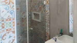 A bathroom with patterned tiles, a shower, and a sink. - Sea view on the beach avenue - Embaré - Santos (Embaré Santos)