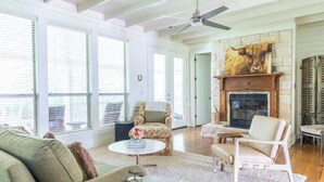 Un salon spacieux doté d’une cheminée, de grandes fenêtres et d’un ventilateur de plafond.