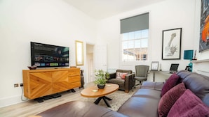 Ein modernes Wohnzimmer mit einem Holz-Fernsehschrank, einem Ledersofa, einem runden Couchtisch und einem großen Fenster.