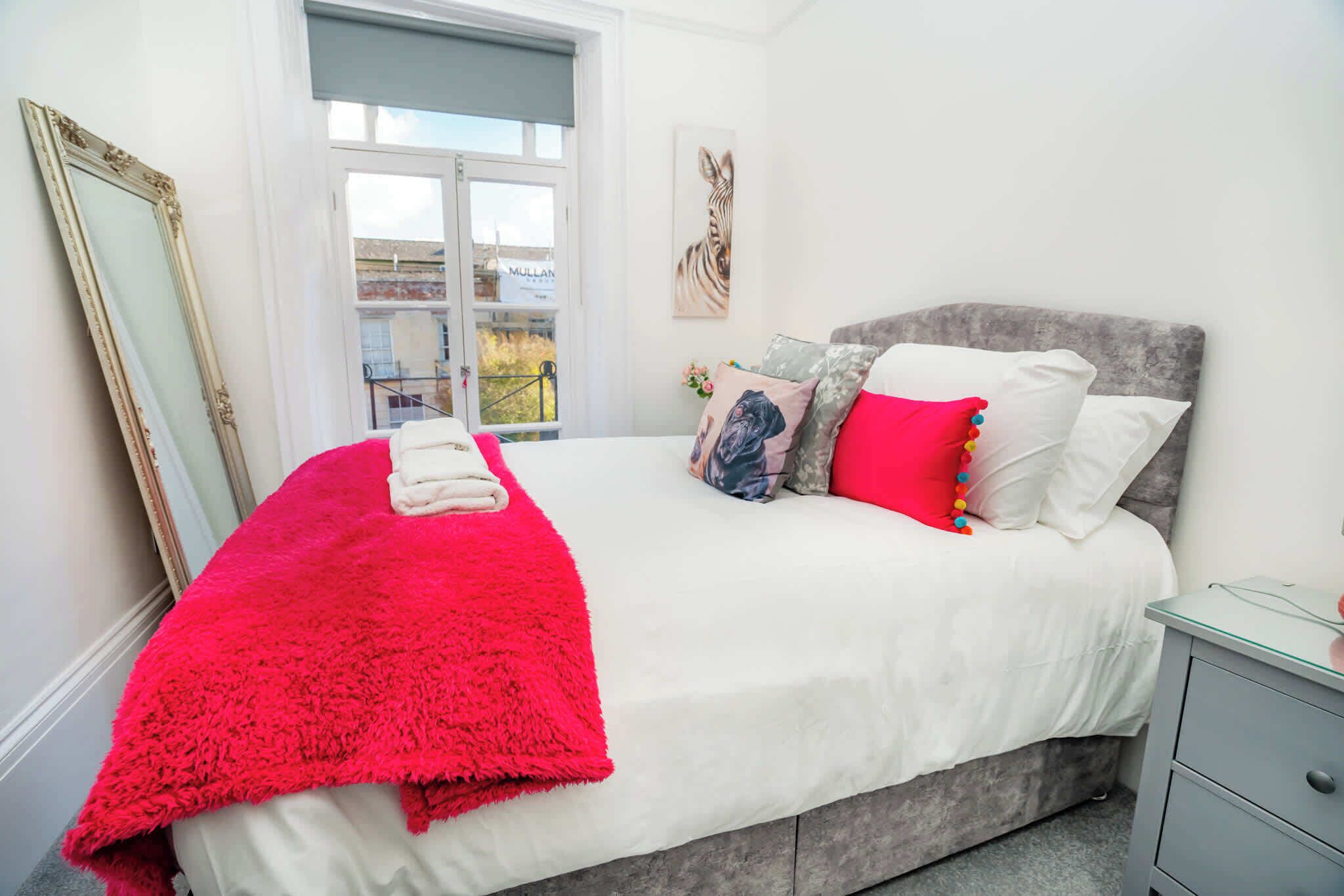 Une chambre à coucher avec un lit, une table de chevet, un miroir et une fenêtre.