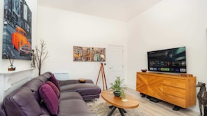 Ein modernes Wohnzimmer mit einem Ecksofa, einem Holztisch, einem Fernseher auf einem Holzständer und einer Hundefigur.