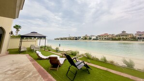 Een balkon met uitzicht op het strand en de oceaan. Er staan ligbedden en een tafel.