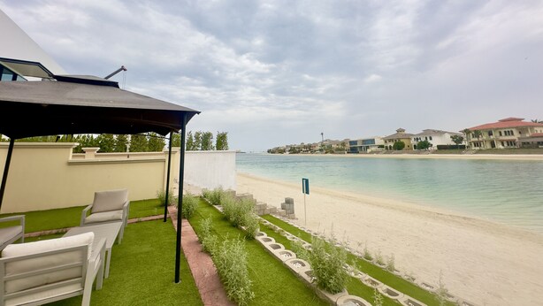 Een terras met buitenmeubilair, een zwembad en uitzicht op het strand en gebouwen.