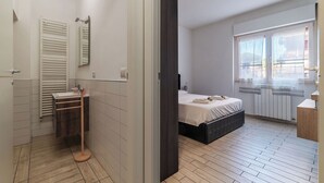 A modern bedroom with a bed, a bedside table, a window, and a bathroom with a toilet, sink, and towel rack. - JOIVY Flat with access to central Rome (Rome)
