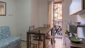 A dining area with a wooden table and chairs, a patterned sofa, and a view of a balcony with outdoor furniture. - JOIVY Flat with access to central Rome (Rome)