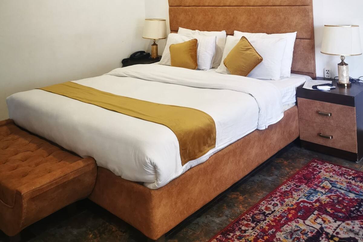 A neatly arranged hotel room with a bed, bedside tables, a nightstand, a small wooden bench, and a ceiling fan.
