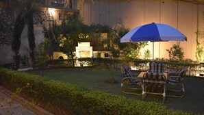An outdoor seating area with a blue umbrella, stone walls, and greenery.
