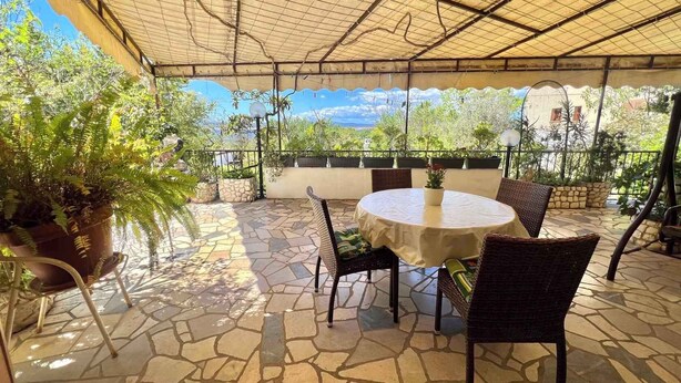 Eine Terrasse im Freien mit Steinboden, Korbstühlen, einem runden Tisch und Topfpflanzen.
