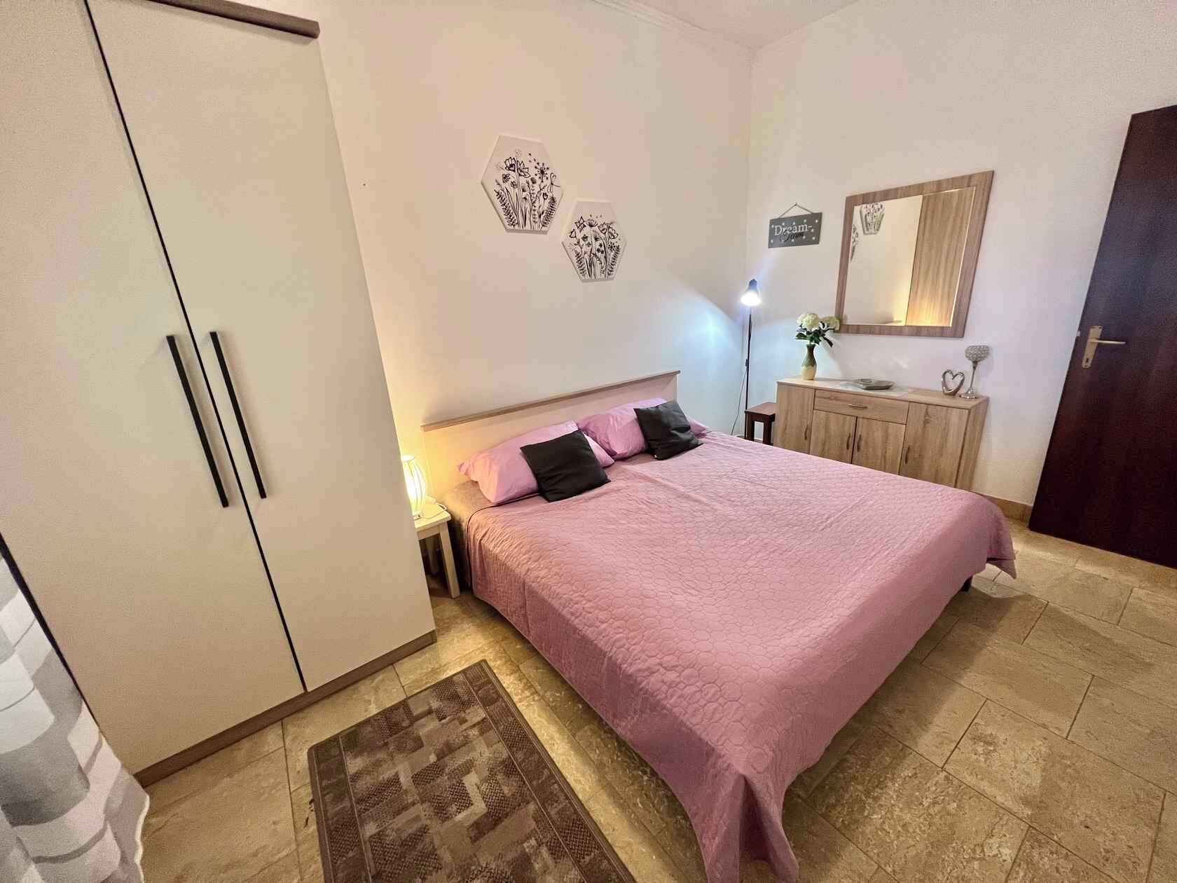 A bedroom with a bed, a wardrobe, a nightstand, a dresser, a mirror, and a rug.