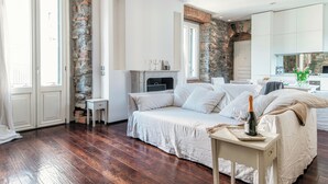 A bedroom with a stone wall, a bed with white linens, a small table with a bottle and glasses, and a fireplace. - Stunning Central Como apt by JOIVY  (Como)
