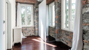 A room with stone walls, wooden flooring, and large windows with curtains. - Stunning Central Como apt by JOIVY  (Como)